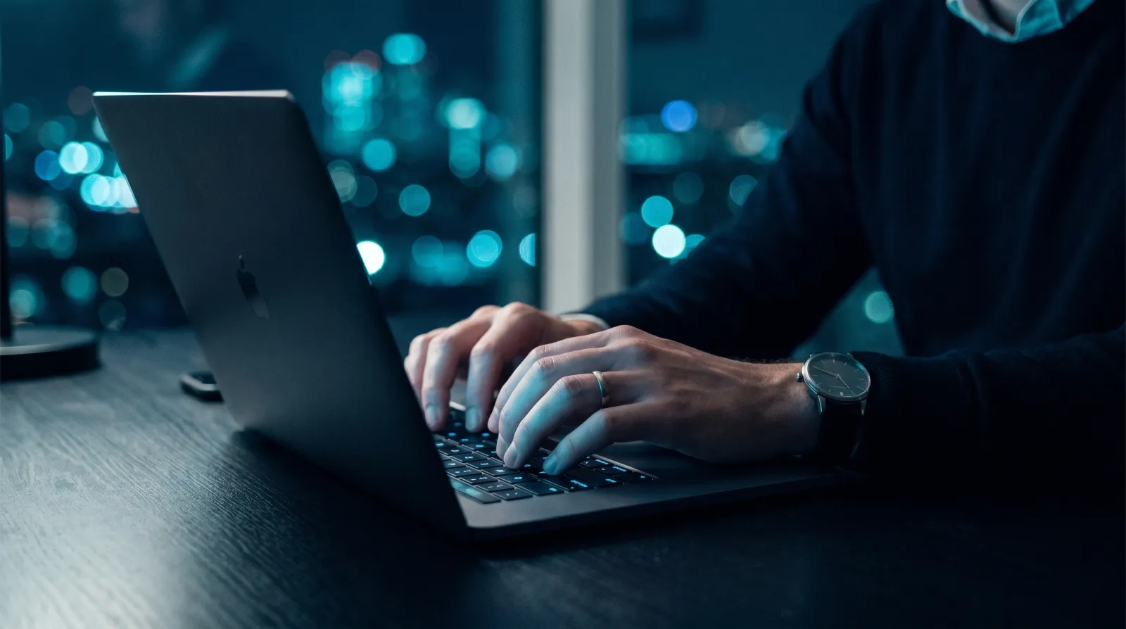Hands typing on a laptop lit by the screen's glow